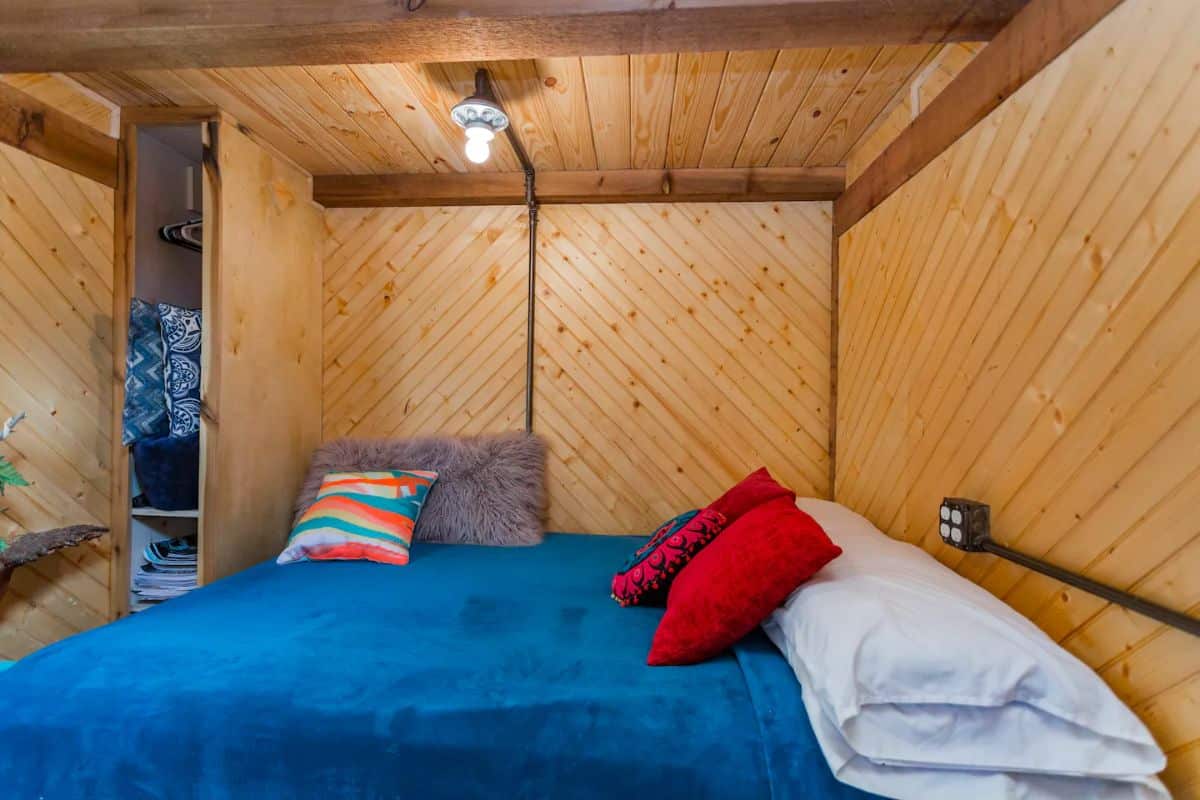 blue bedding on bed tucked underneath loft at back of tiny home