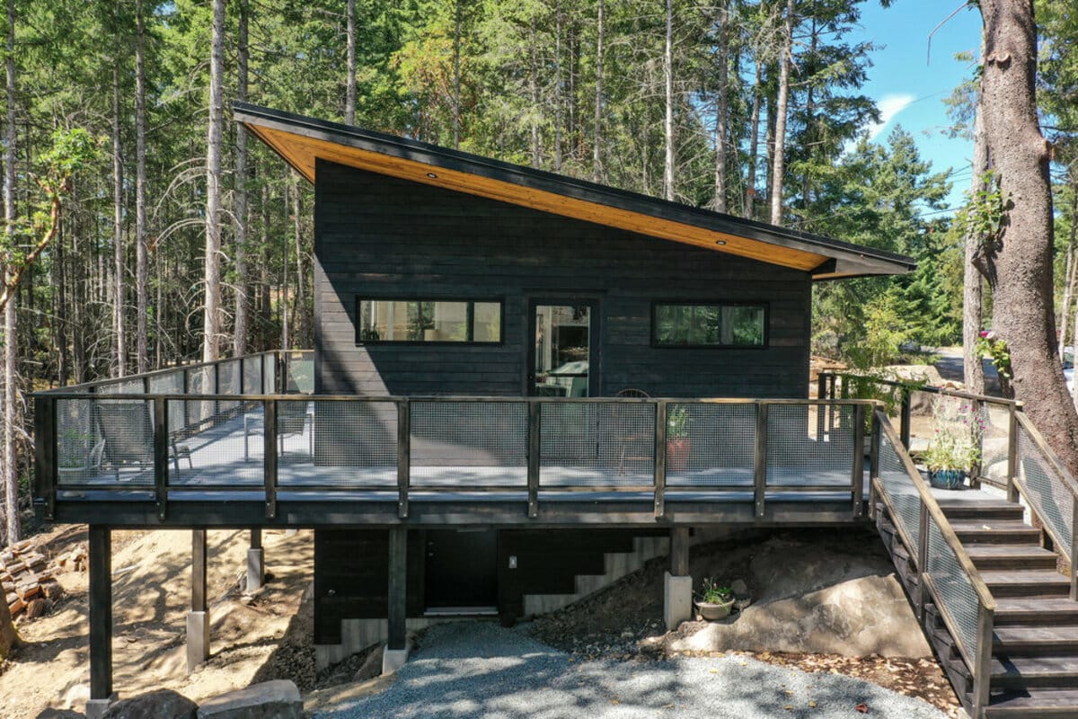 Exterior of cabin with steps up to deck, sloped roof with overhang, and visible footers and foundation