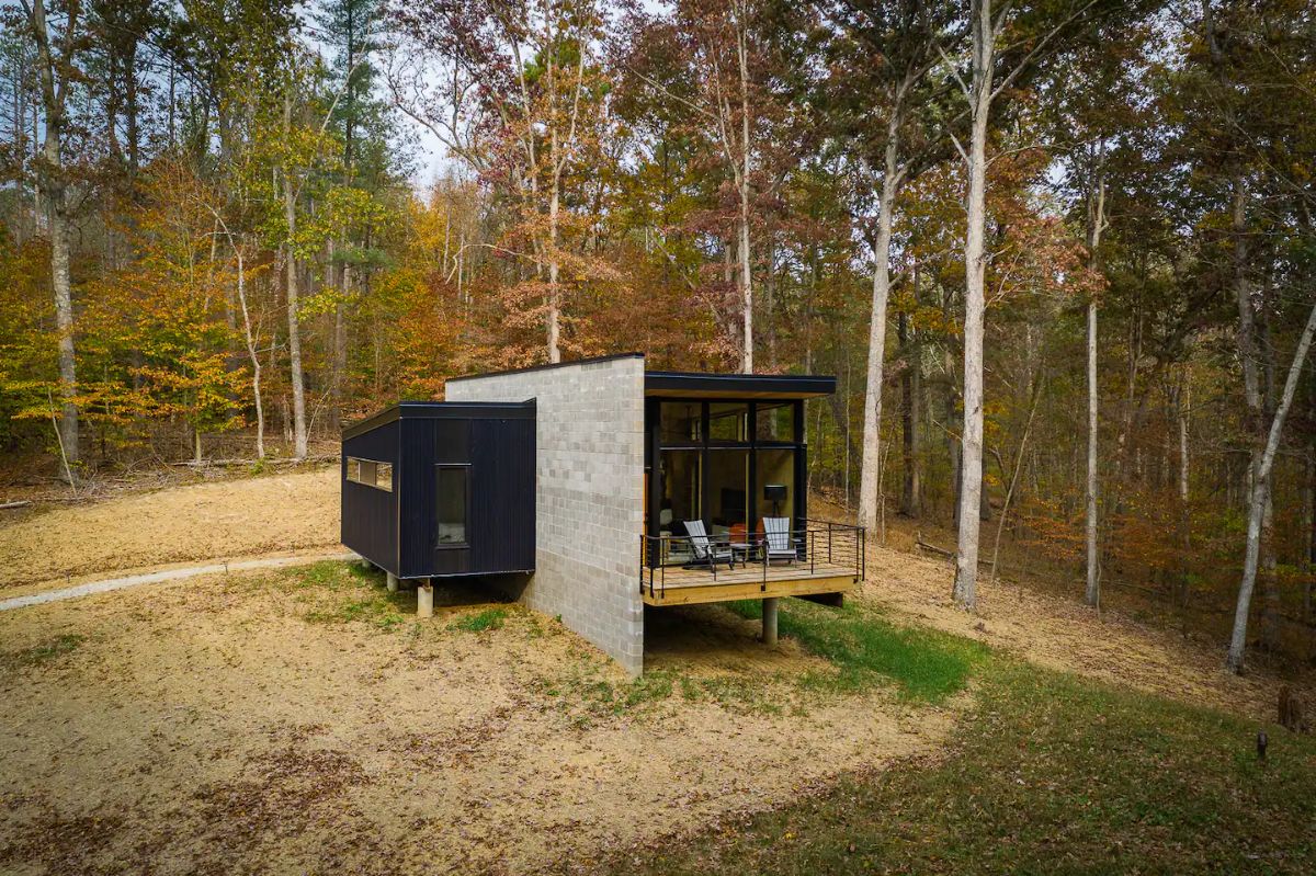 black and concrete tiny home in field with treeline in background
