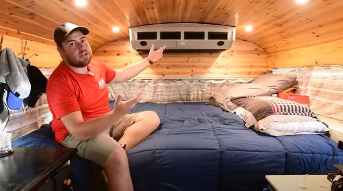 man in red shirt sitting on blue bed at back of tiny home school bus