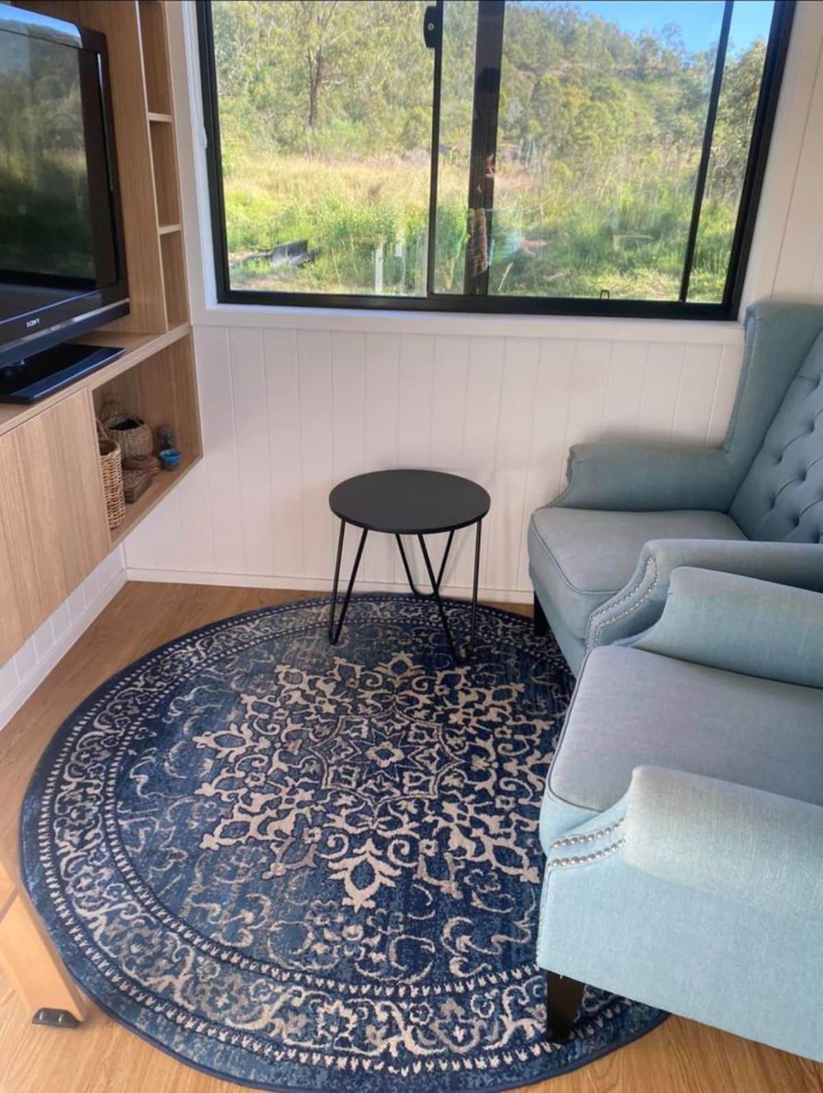 Living area of sustainable tiny home has a couch, center table and wall mounted tv set