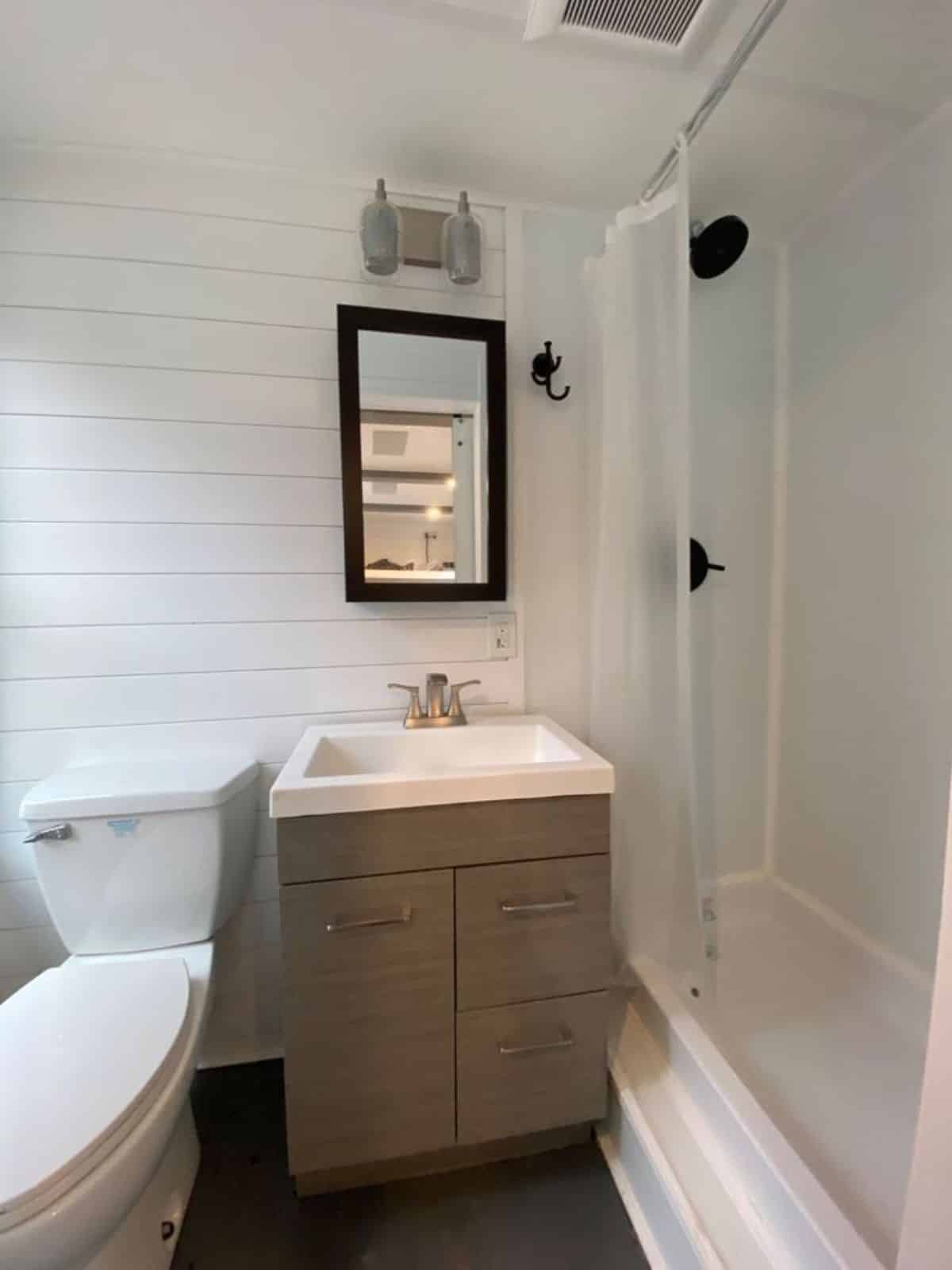Bathroom area of solar powered tiny home has standard toilet, sink with vanity & mirror and shower area