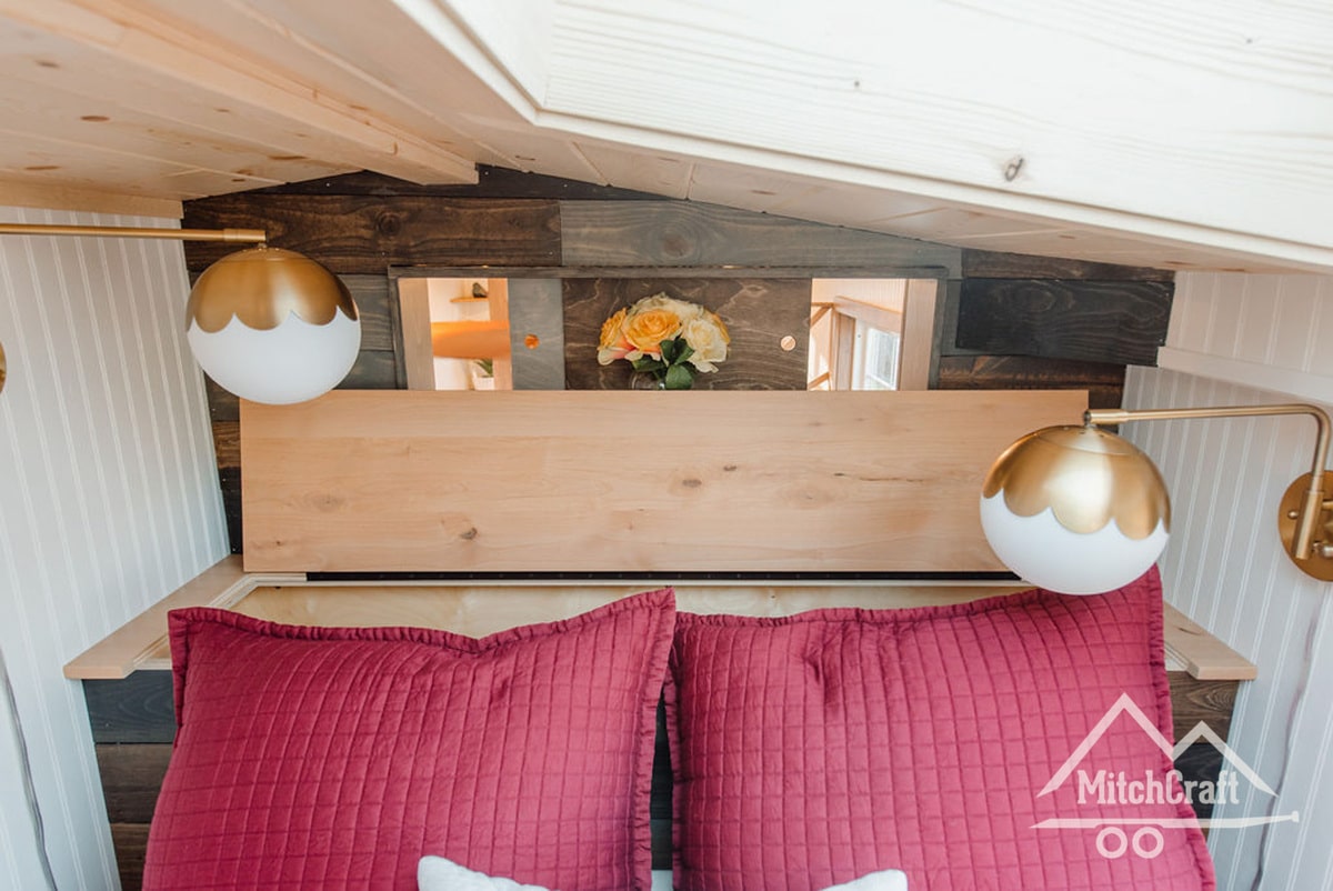 A view of the sleeping area headboard, featuring a natural rustic reclaimed wood board mosaic along the back wall, slide panels in this headboard back wall that allow for a view down into the rest of the dwelling, and a flip-up cover on the built-in headboard storage chest.