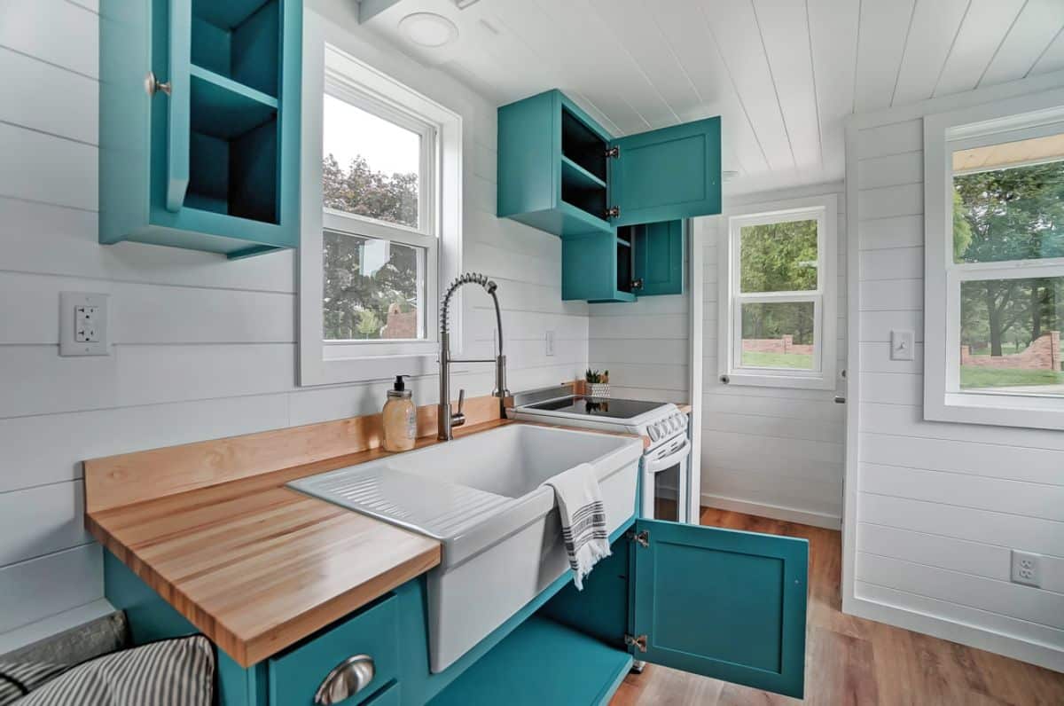white farmhouse sink in butcher block countertop with open teal counters below
