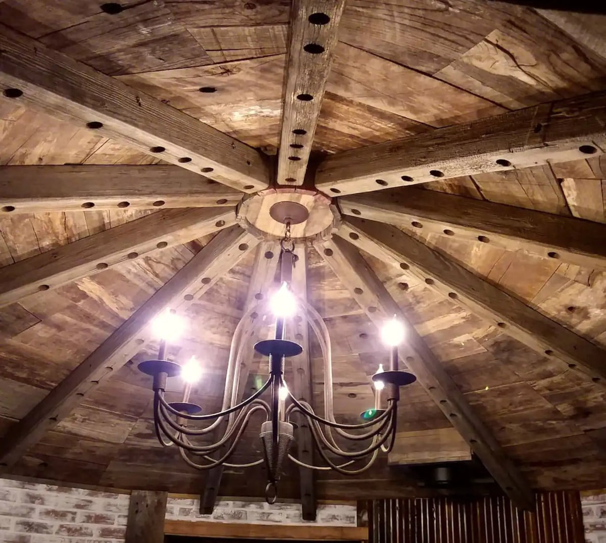 Reclaimed wood slats and timbers on ceiling with rustic chandelier in center