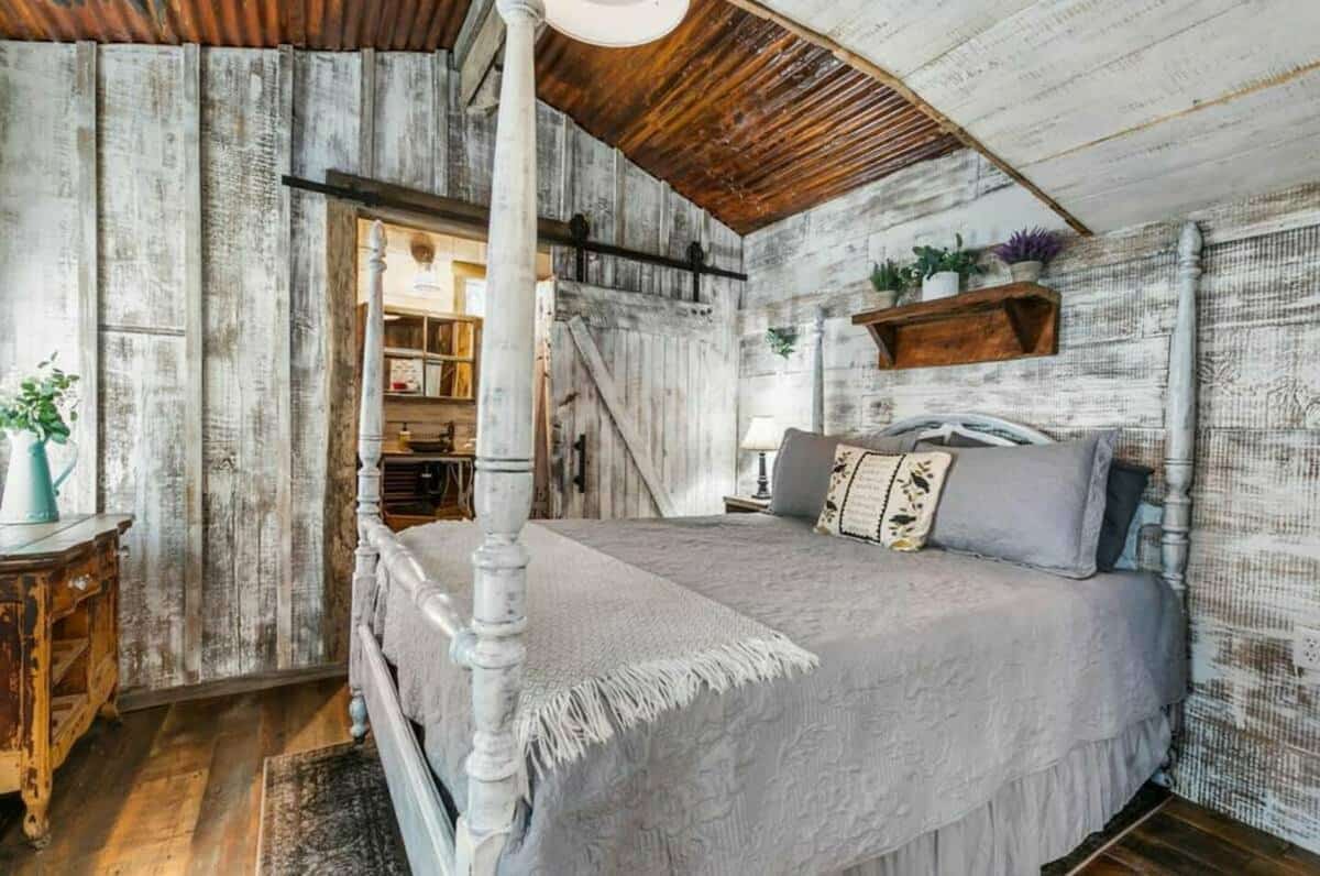 Cozy sleeping area with reclaimed barn board siding, 4 post bed, and rustic rusty corrugated siding on ceiling