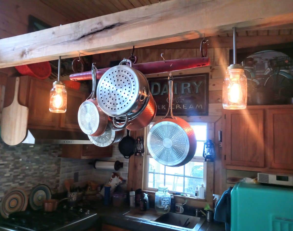 Ray’s Cabin Off-the-Grid Tiny House kitchen ware and jar lights hanging on a log.
