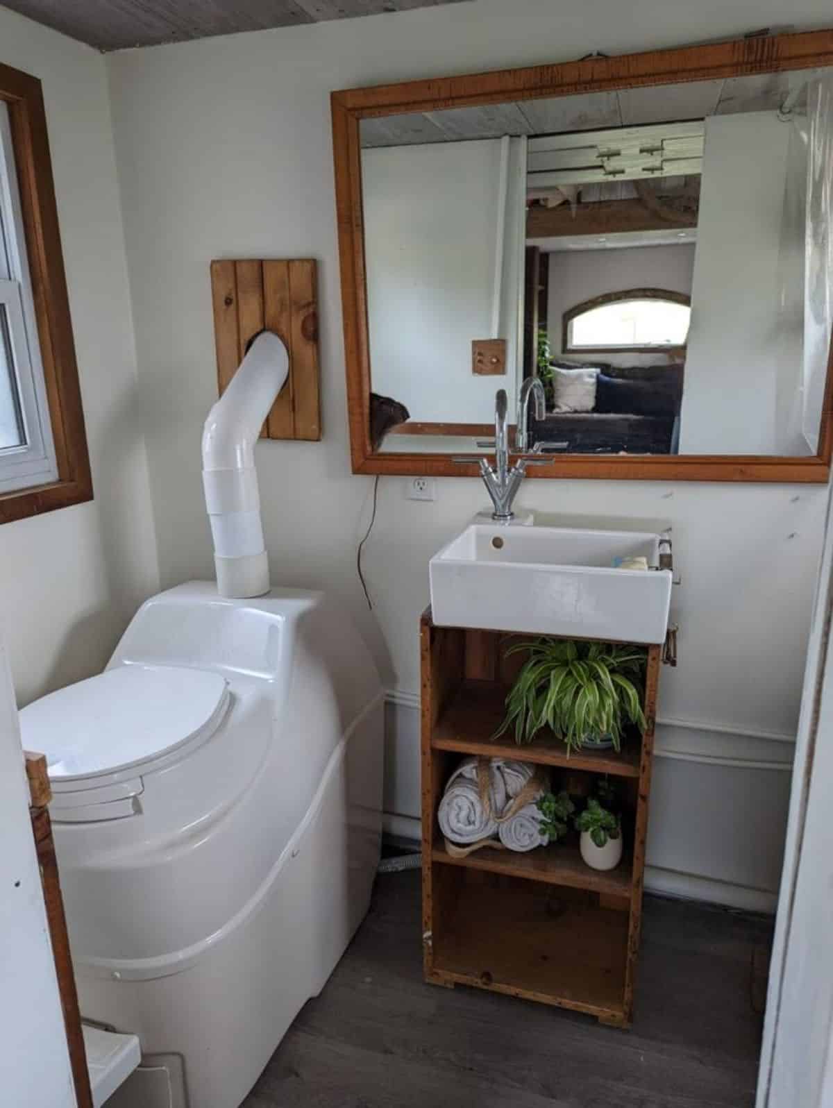 bathroom of off grid tiny home has a composting toilet, sink with vanity & mirror