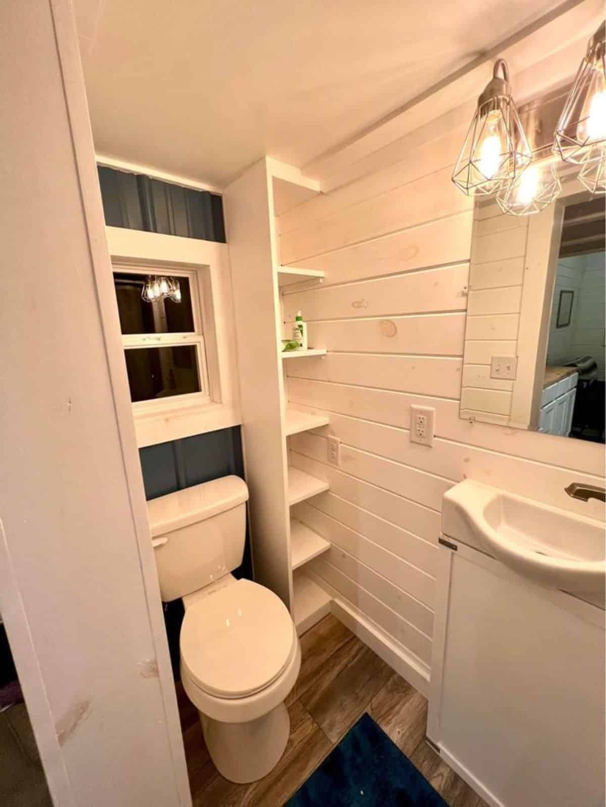 Standard toilet, sink with vanity and mirror and side racks in bathroom
