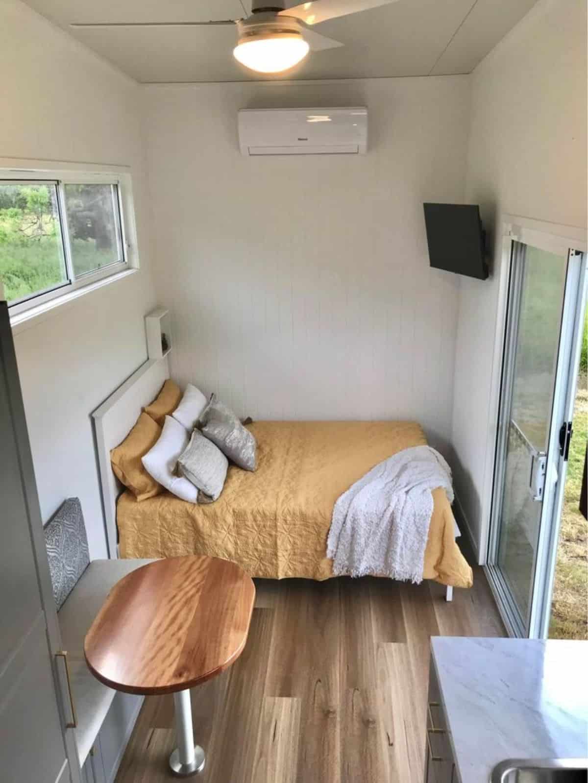 Open bedroom with comfortable double bed and wall mounted TV set in open area of furnished tiny house