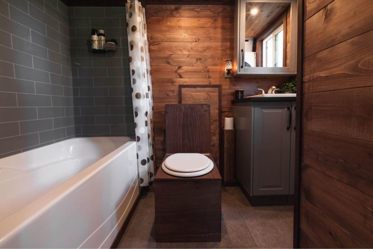 bathroom of 30' tiny house on wheels has a composting toilet, sink with vanity and mirror and a huge bathtub
