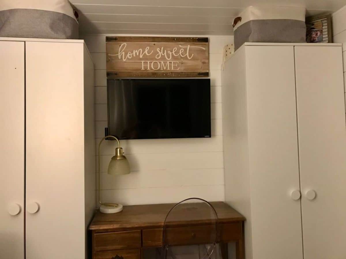 storage cabinets and wall mounted TV set is installed in the main floor bedroom area of fully furnished tiny home