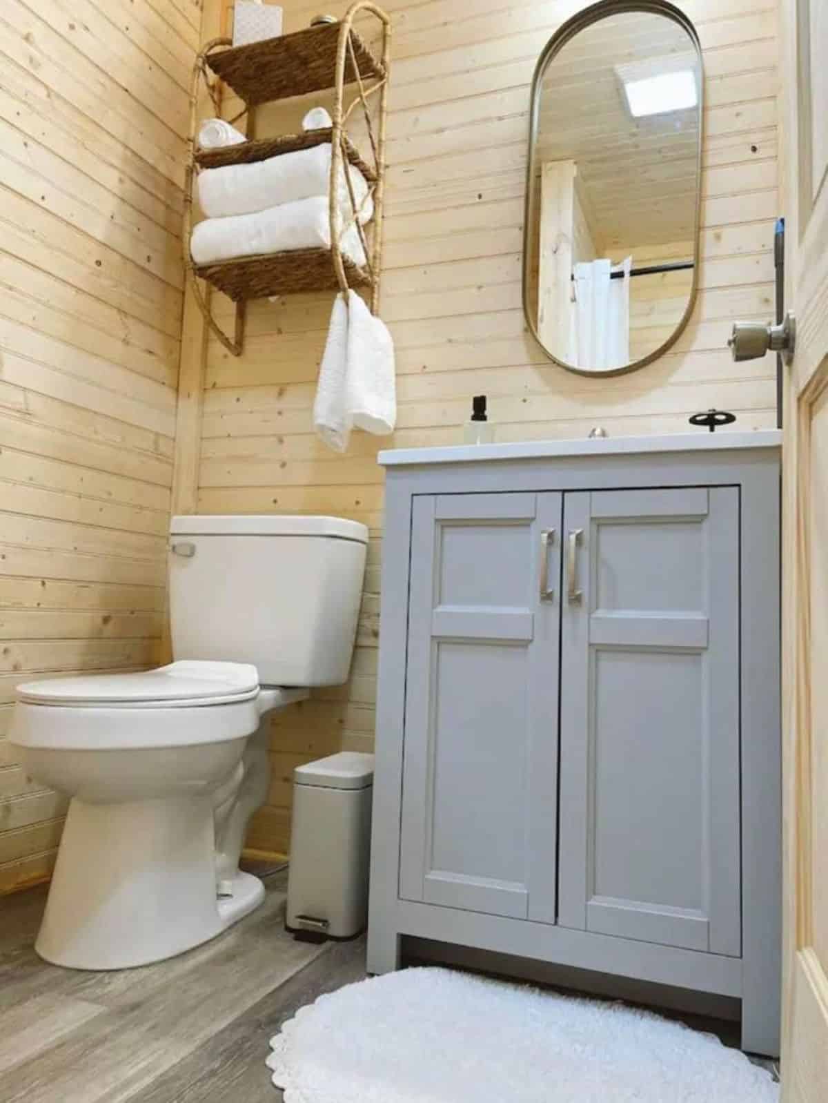standard toilet, sink with vanity and mirror in bathroom of 24’ tiny home