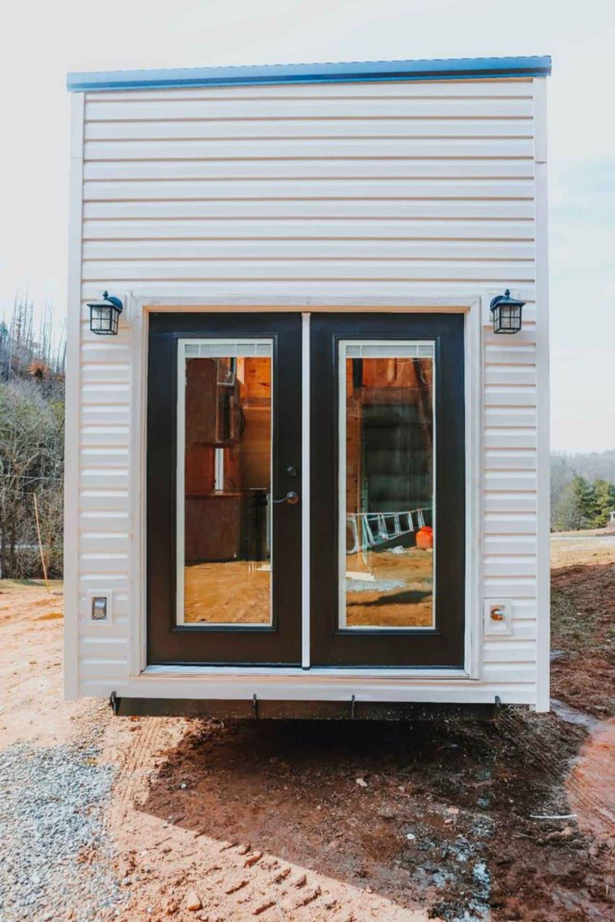 main glass entrance view and stunning white exterior of spacious tiny house on wheels