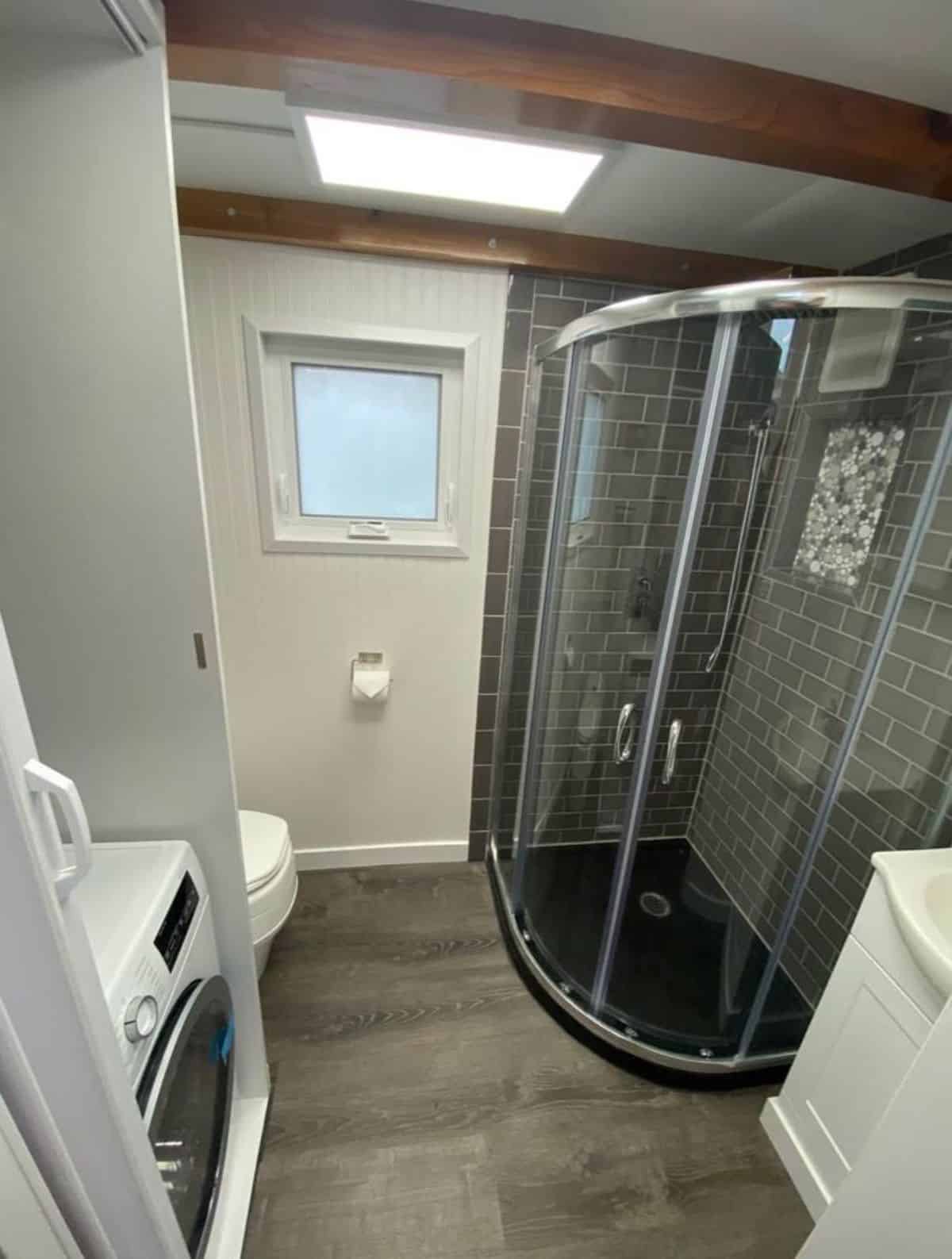 bathroom of 24' towable tiny home is spacious with standard fittings, separate shower with glass enclosure and washer dryer combo