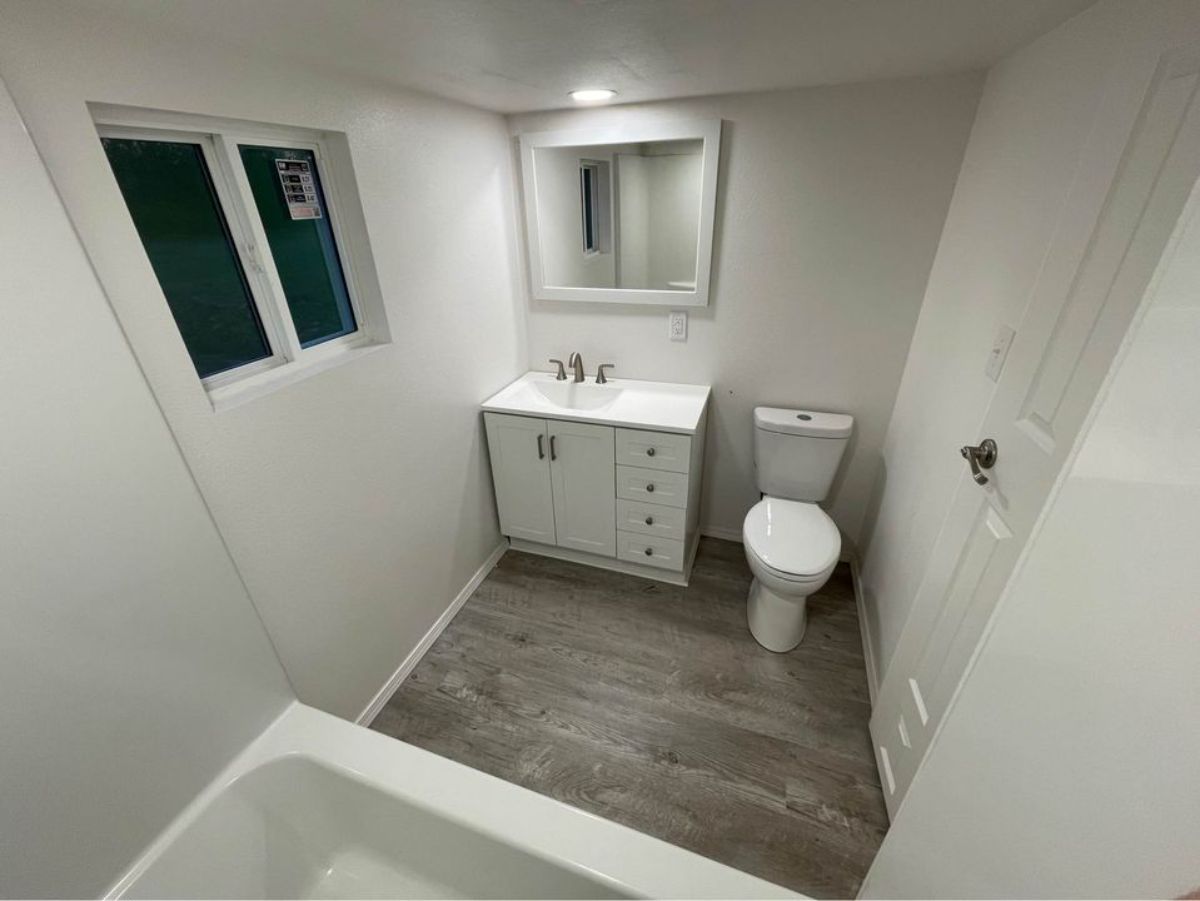 sink with vanity and mirror, still ample space left to roam in bathroom of 24’ modern tiny home