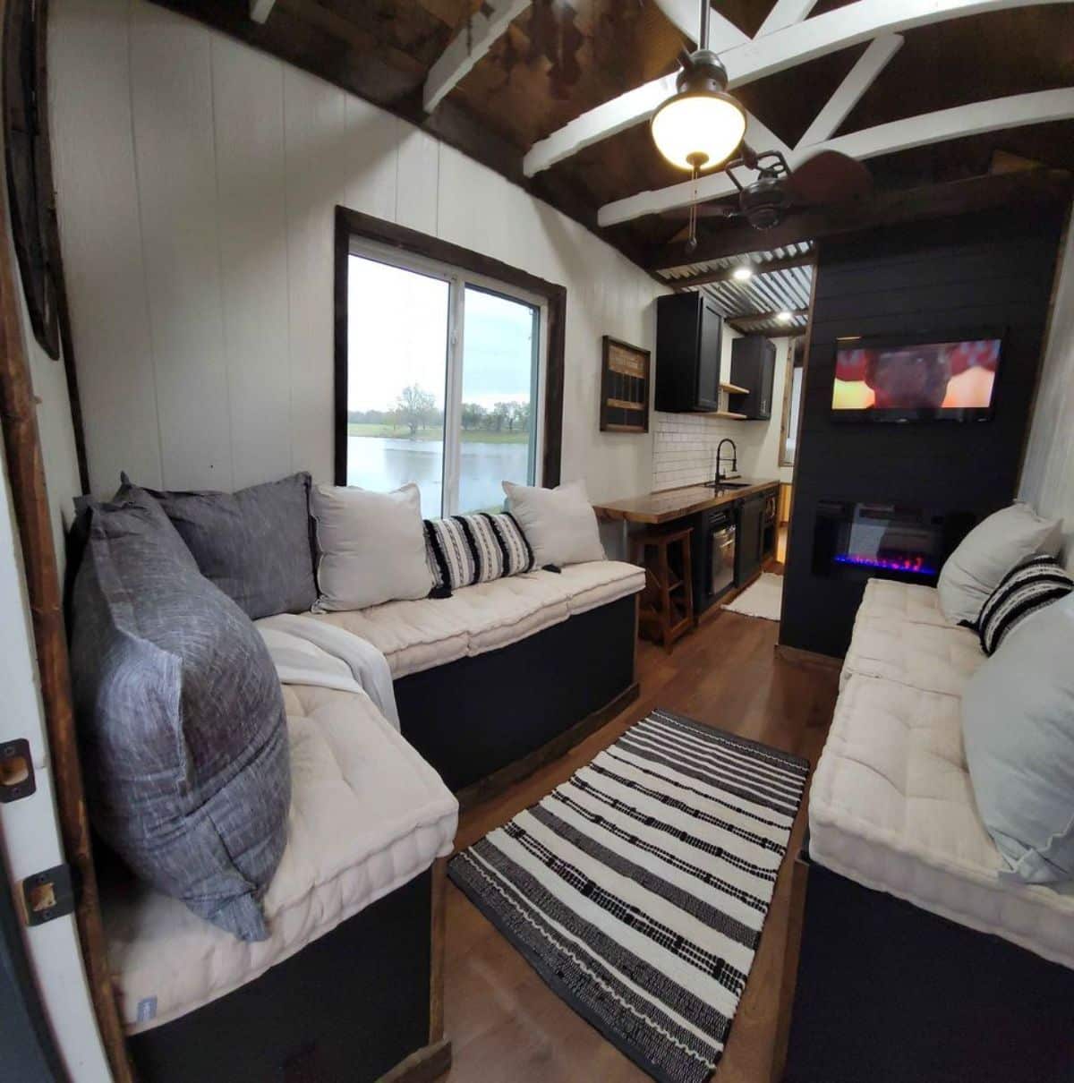 L shaped couch with TV set and an electric fireplace in living area of 25' tiny house on wheels