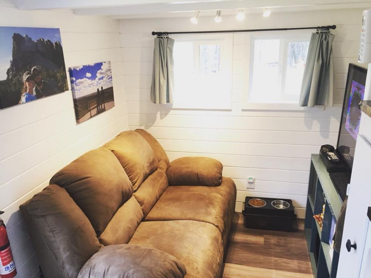 living area of Noah certified tiny house has a three seater couch, walls mounted Tv and an entertainment unit with a window