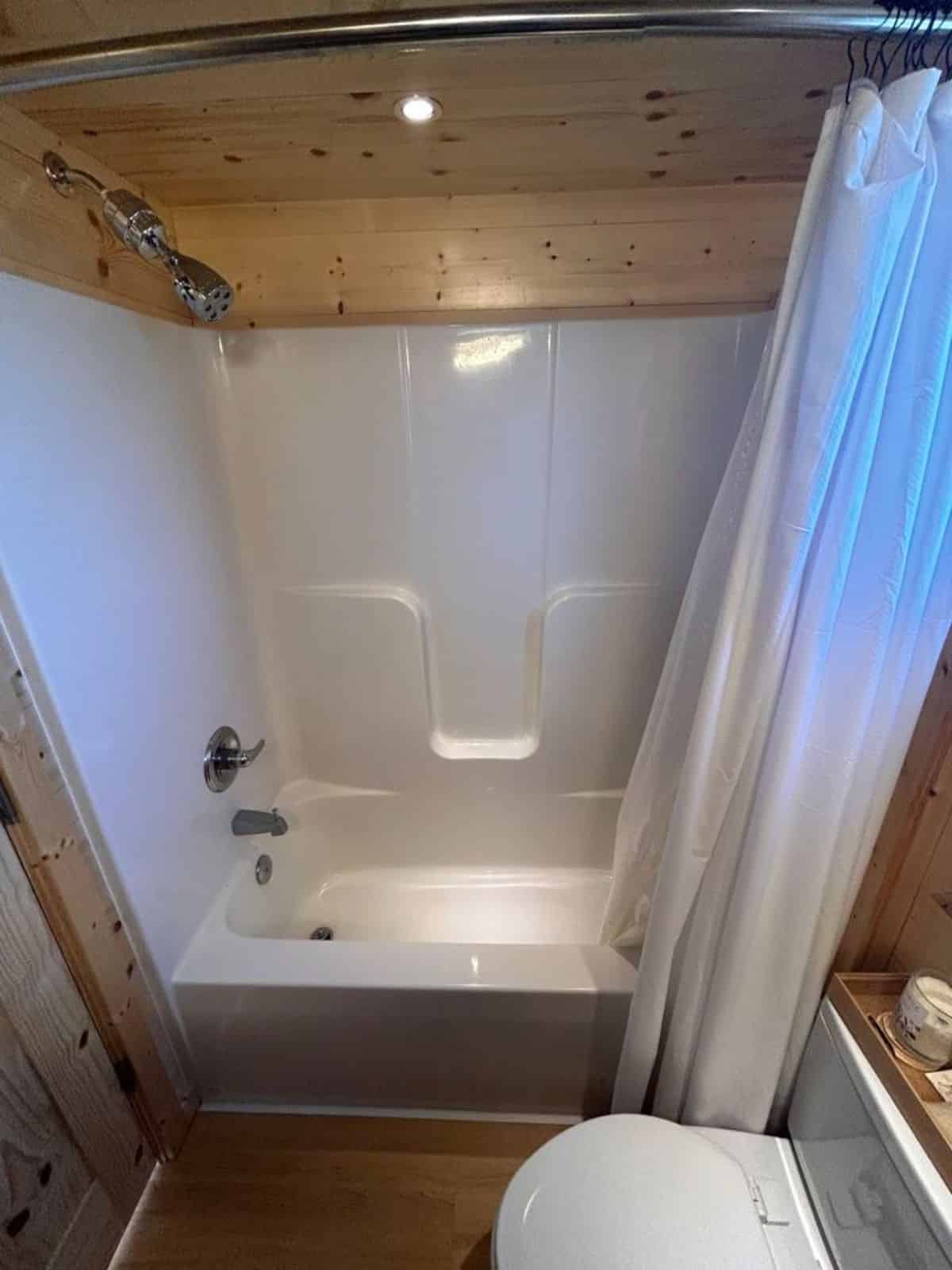 bathtub with full length shower in bathroom of certified tiny home