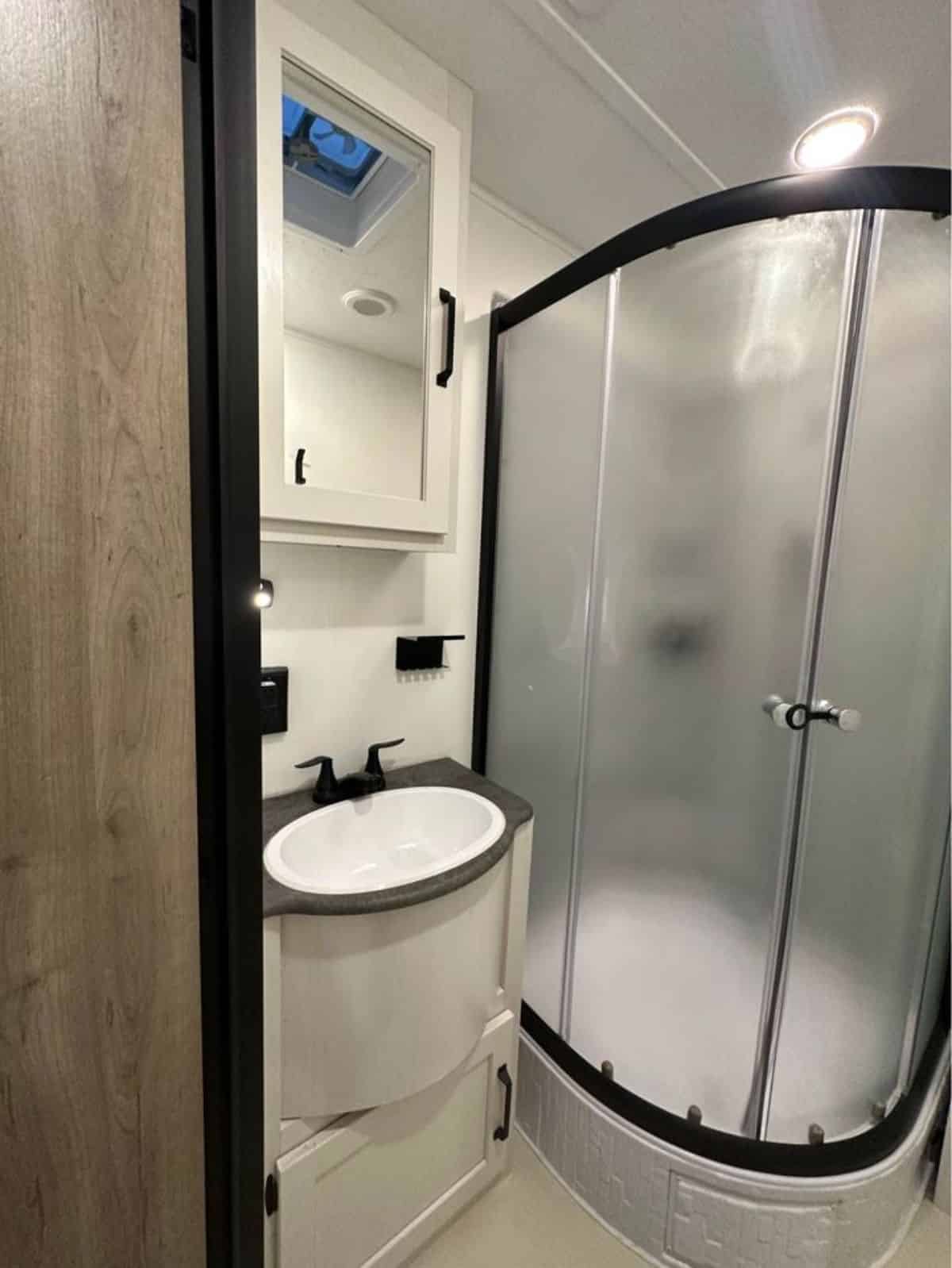 bathroom of upgraded tiny home has all the standard fittings and separate shower area with glass enclosure