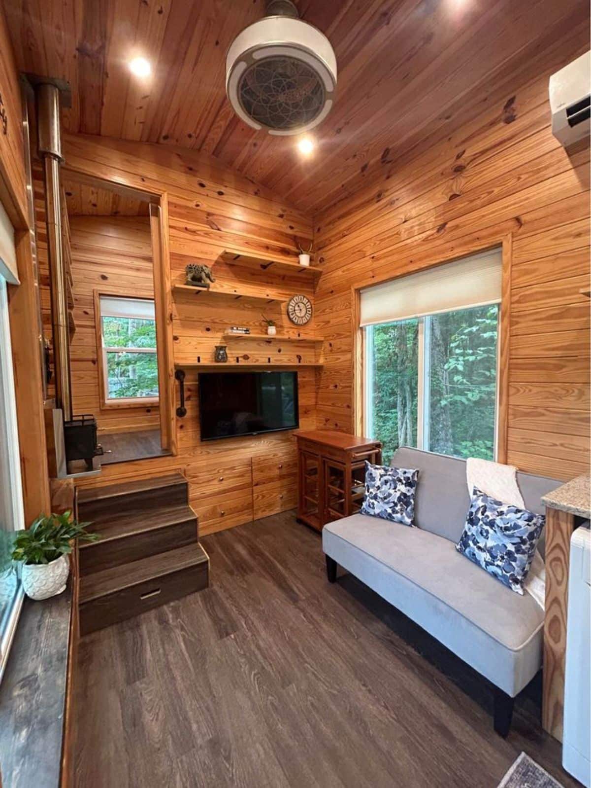 living area of 26’ custom tiny home has a couch, side table and wall mounted TV set