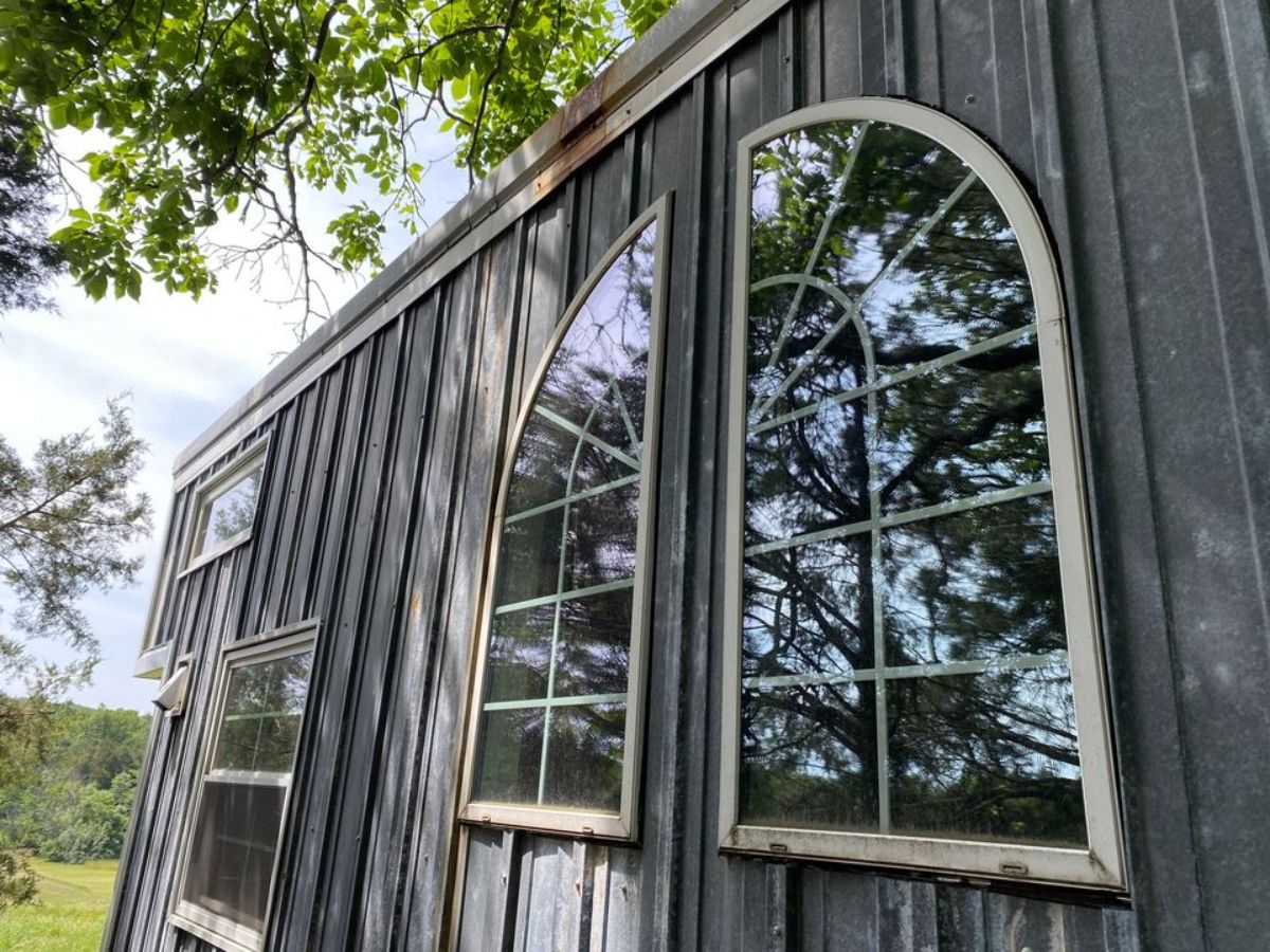 stunning huge windows and black wooden exterior of 20’ rustic tiny house