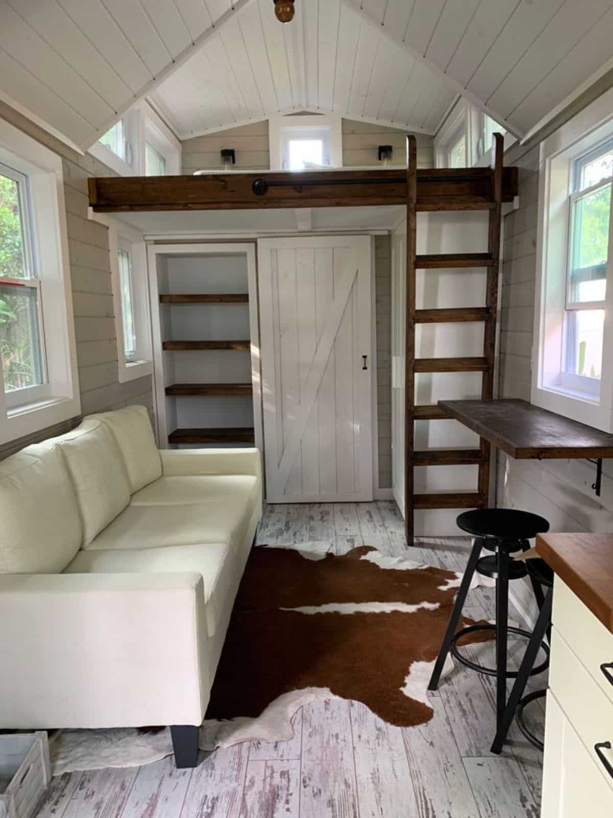 living area has a couch besides another window of furnished tiny home