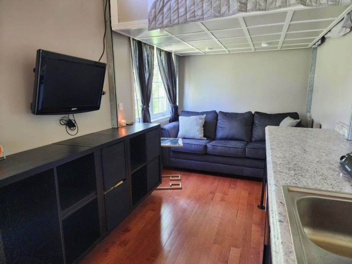 living area has a 3 seater couch besides the window  and an entertainment unit with wall mounted TV set