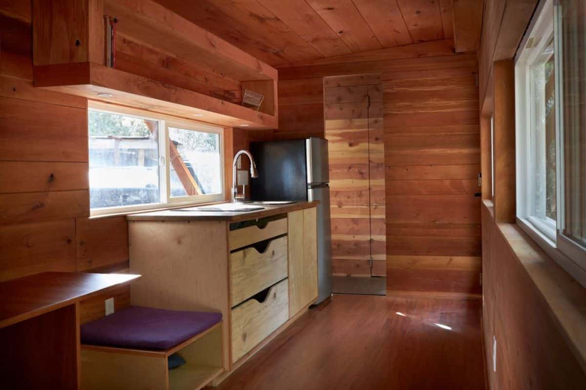 single countertop with storage in kitchen area with huge window of 22' rustic tiny house